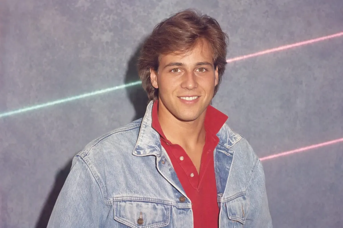 Studioporträt eines jungen Mannes von 1986: gefönte Haare, Stonewashed-Jeansjacke über rotem Polohemd, blau melierter Hintergrund