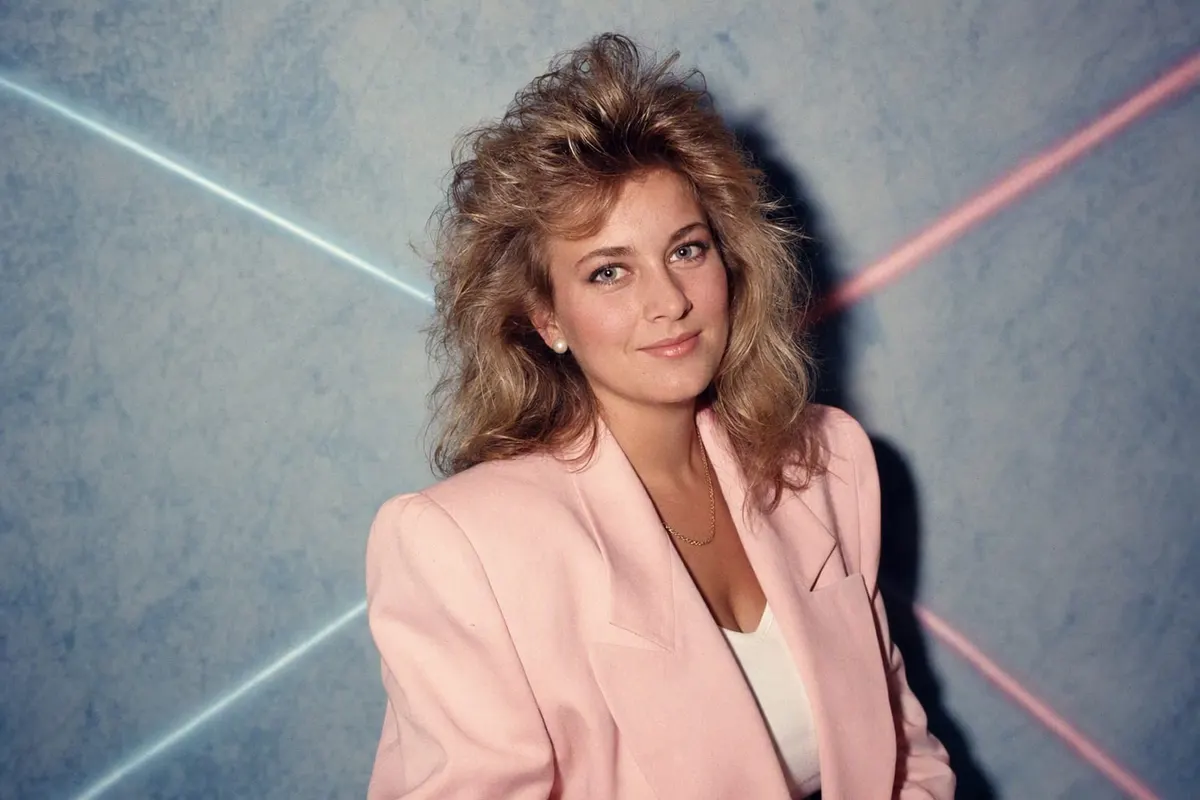 Studioporträt im 80er-Trend: Föhnwelle, pastellrosa Blazer mit Schulterpolstern, blau melierter Hintergrund mit Laserstrahlen und hartes Blitzlicht