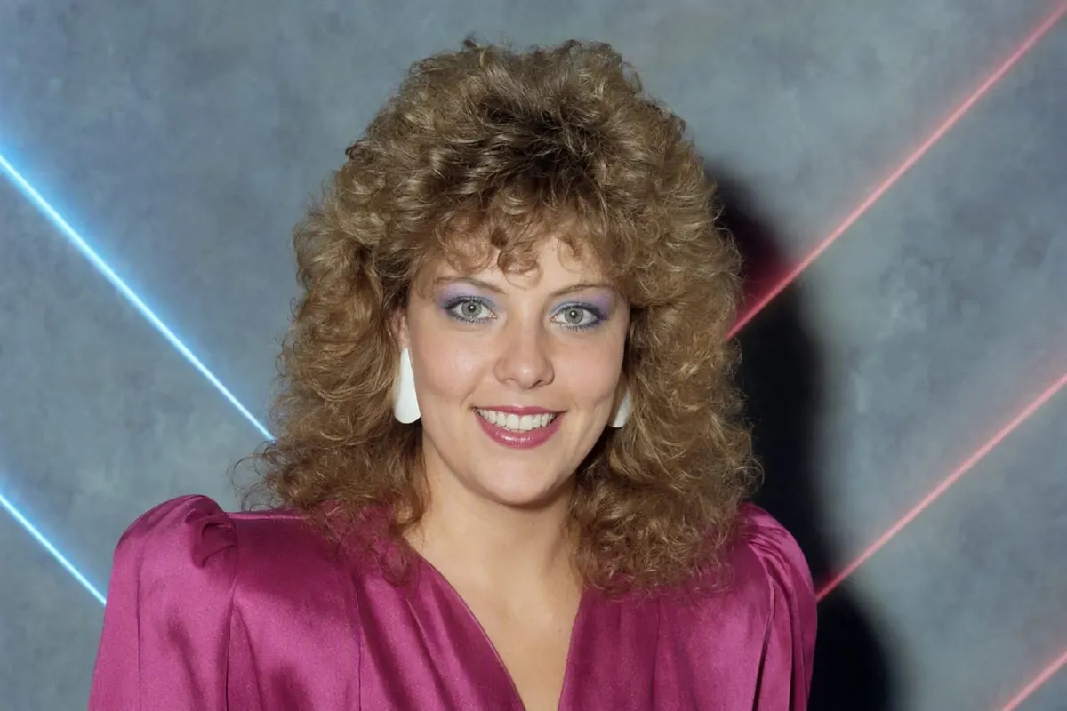 1986 studio portrait of a young woman with permed hair and a magenta satin blouse against a mottled blue backdrop with laser streaks