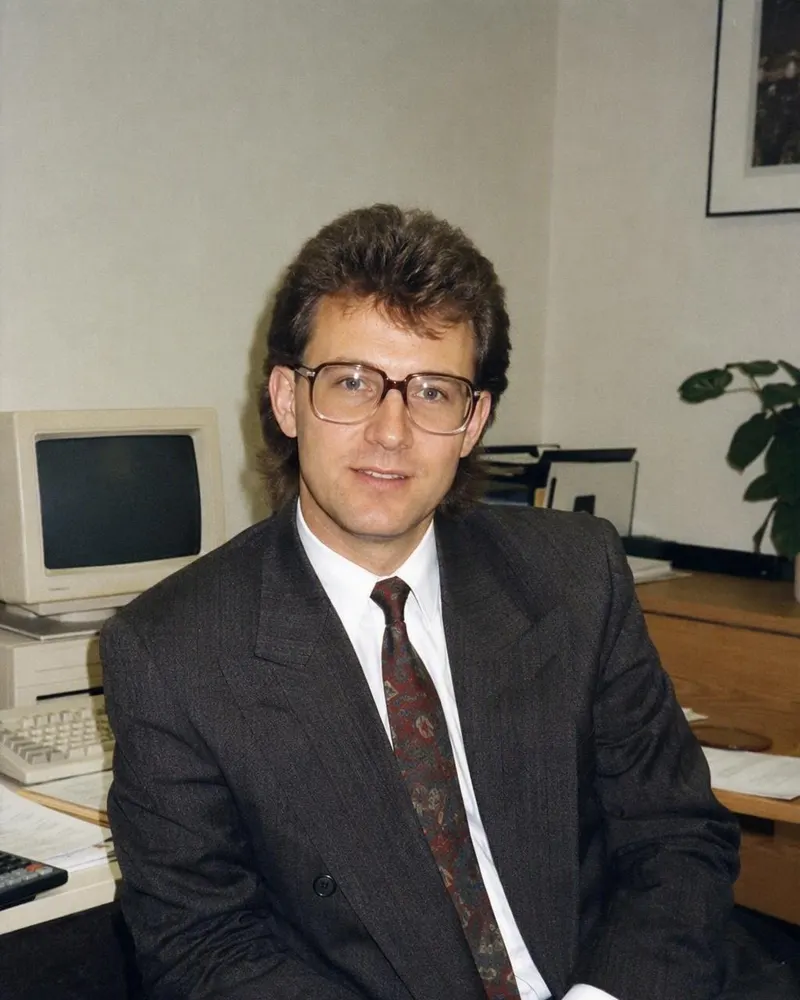 El retrato de oficina, con traje de hombreras y lentes de armazón grande.