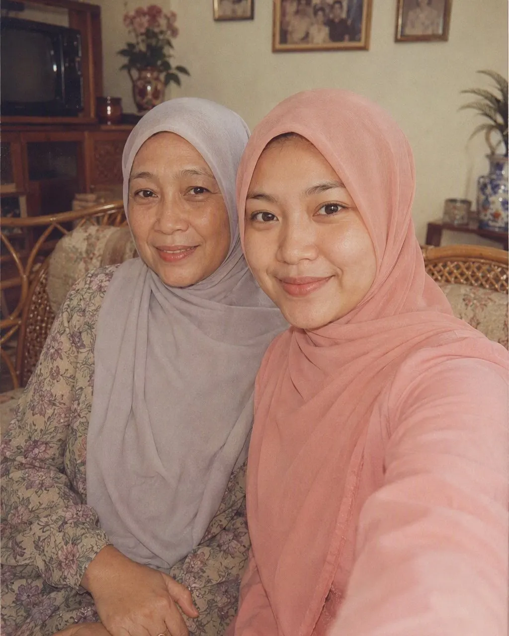 Ibu dan anak perempuannya di sofa, sama-sama berhijab modern, lalu versi 80-annya: gaun lengan panjang dan kerudung longgar yang tetap menutup rambut, di ruang tamu dengan kursi rotan dan foto keluarga berbingkai.