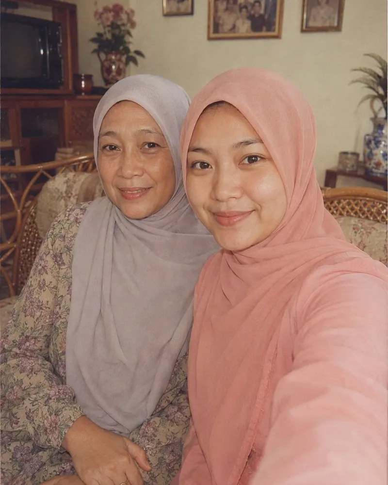 Foto ibu dan anak di sofa jadi potret keluarga tahun 80-an: dress lengan panjang, kerudung longgar yang tetap menutup rambut, dan foto keluarga berbingkai di dinding.
