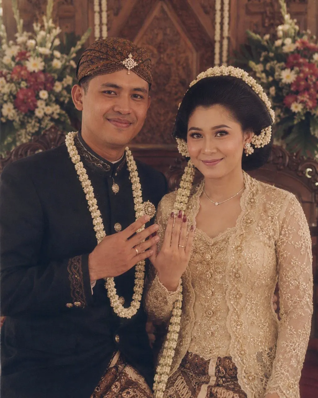 Pengantin Jawa tahun 80-an: kebaya bordir dengan kain batik dan sanggul melati, beskap dengan blangkon, di pelaminan kayu ukir