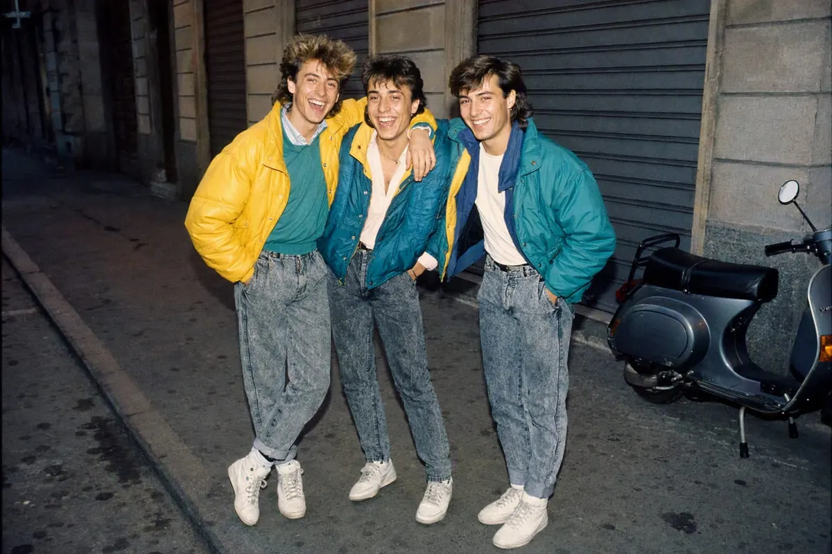 Tre amici in piumino da paninari su una strada di Milano nel 1986, flash diretto e grana della pellicola: esempio di foto anni 80 generata con l’AI e pubblicata su Instagram