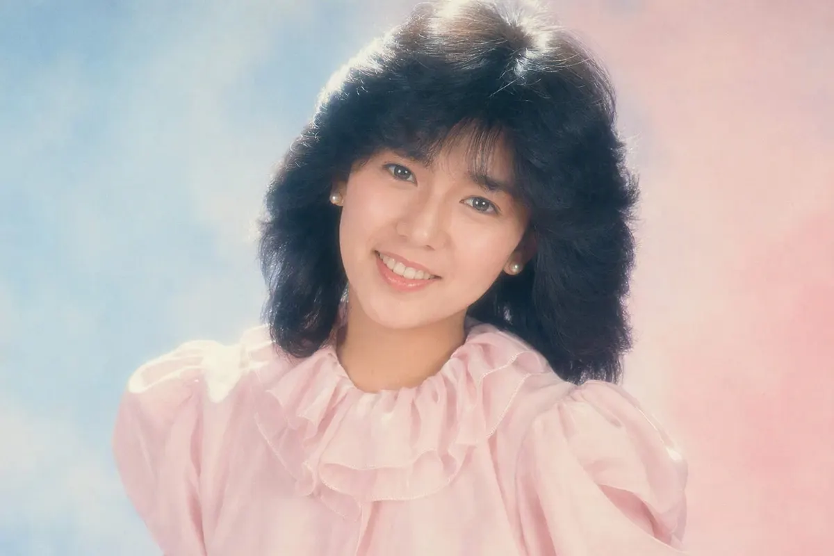 1986年ごろの昭和アイドル風ポートレート。パステルのグラデーション背景、ソフトフォーカス、段の入ったふんわりヘア、ピンクのフリルブラウス