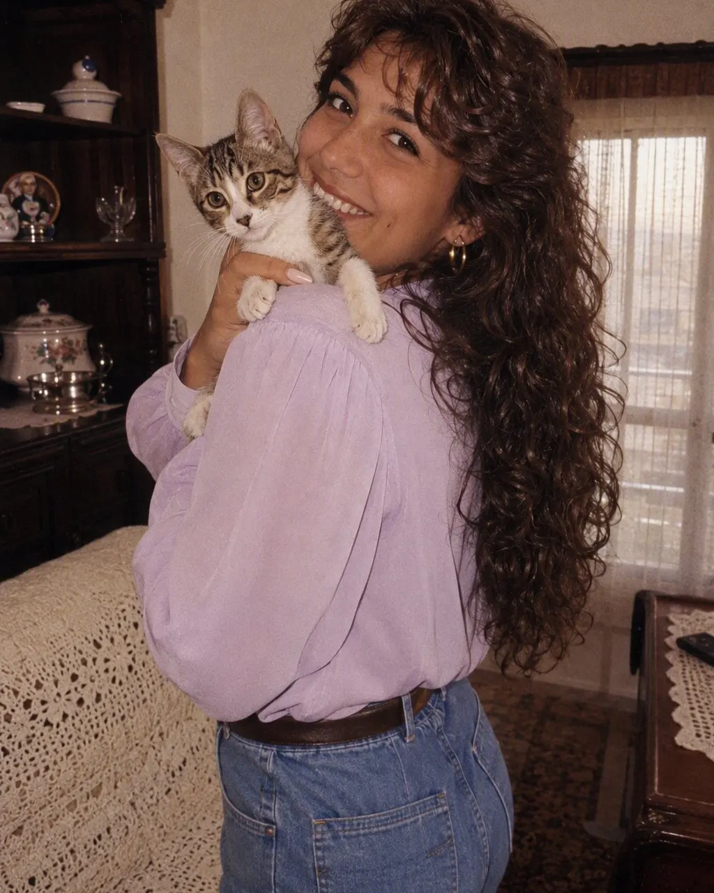 Pessoa com um gato ao colo num sofá castanho, em fotografia com aspeto antigo