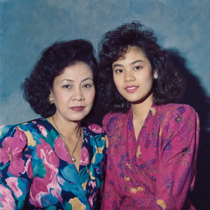 ภาพแม่กับลูกสาววัยผู้ใหญ่บนโซฟา กลายเป็นภาพงานรวมญาติช่วงสงกรานต์กลางยุค 80 ผ้าปูโต๊ะลูกไม้ ตู้โชว์ไม้ เสื้อลายดอกแขนยาว และแสงแฟลชที่ทิ้งเงาสั้น ๆ ไว้หลังไหล่