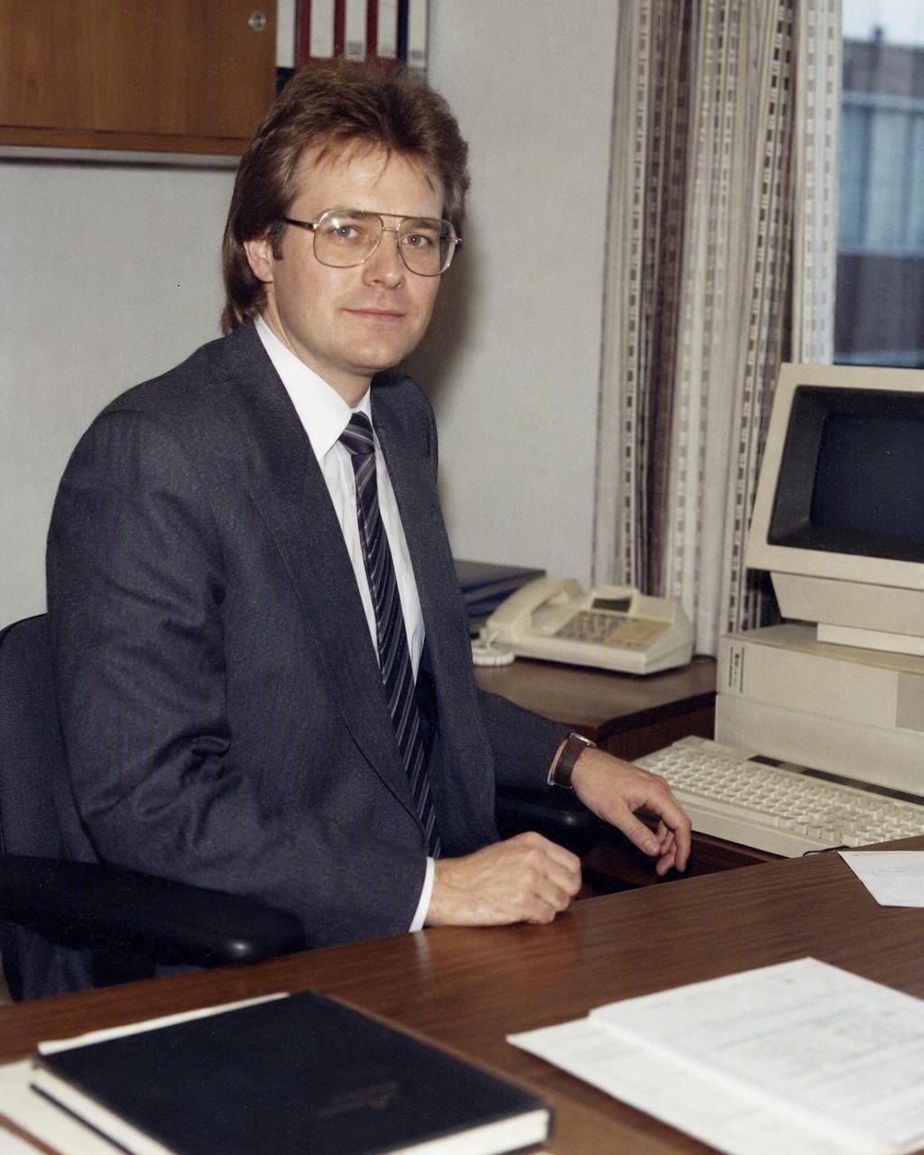 Et kontorportrett i stil fra midten av 1980-tallet med dress med brede skuldre og store brilleinnfatninger